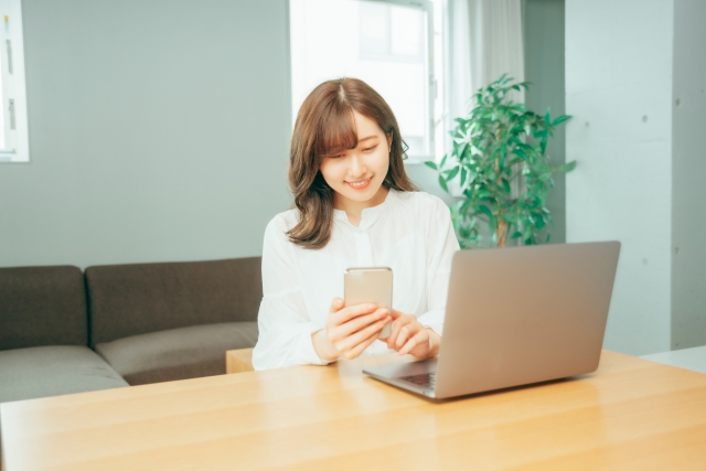 スマホを片手に微笑む女性の画像